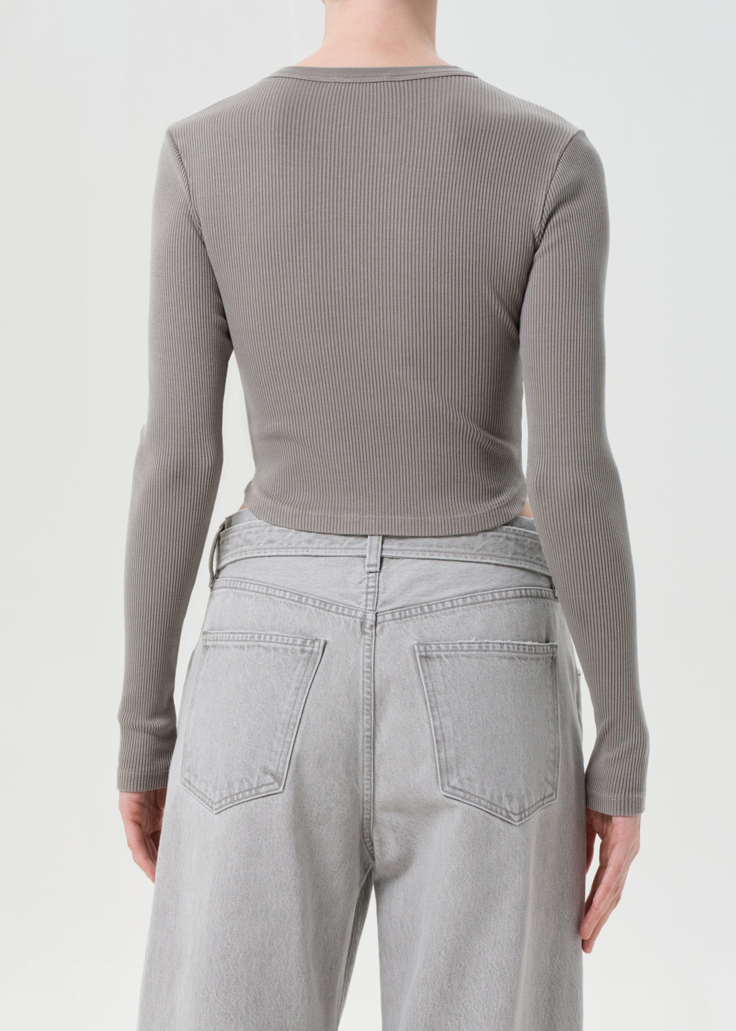 Person wearing a gray ribbed long-sleeve top and light gray jeans on a white background