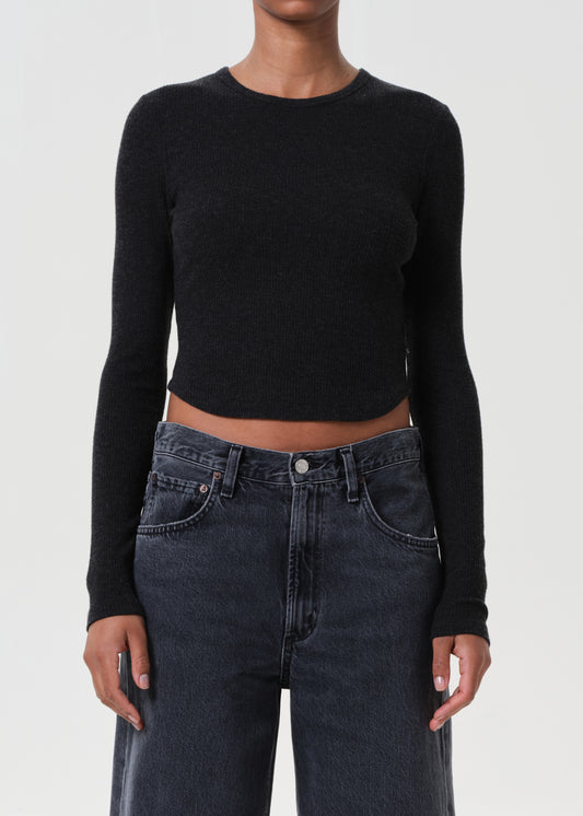 Person wearing a black long-sleeve crop top and dark jeans on a white background
