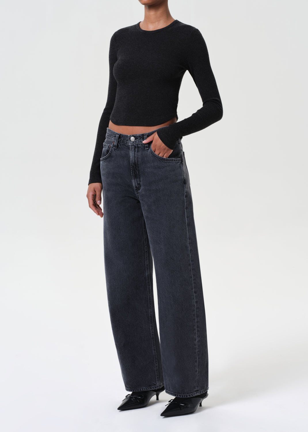 Person wearing a black long-sleeve top and dark blue jeans on a white background