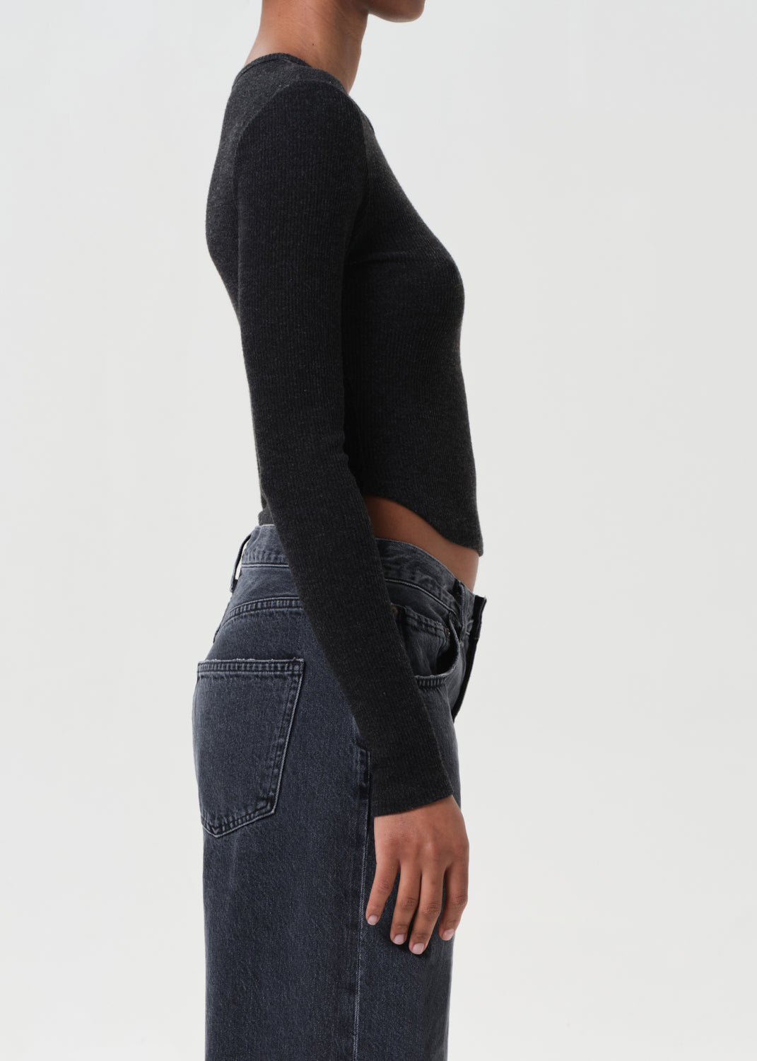 Person wearing a black long-sleeve top and dark jeans on a light gray background