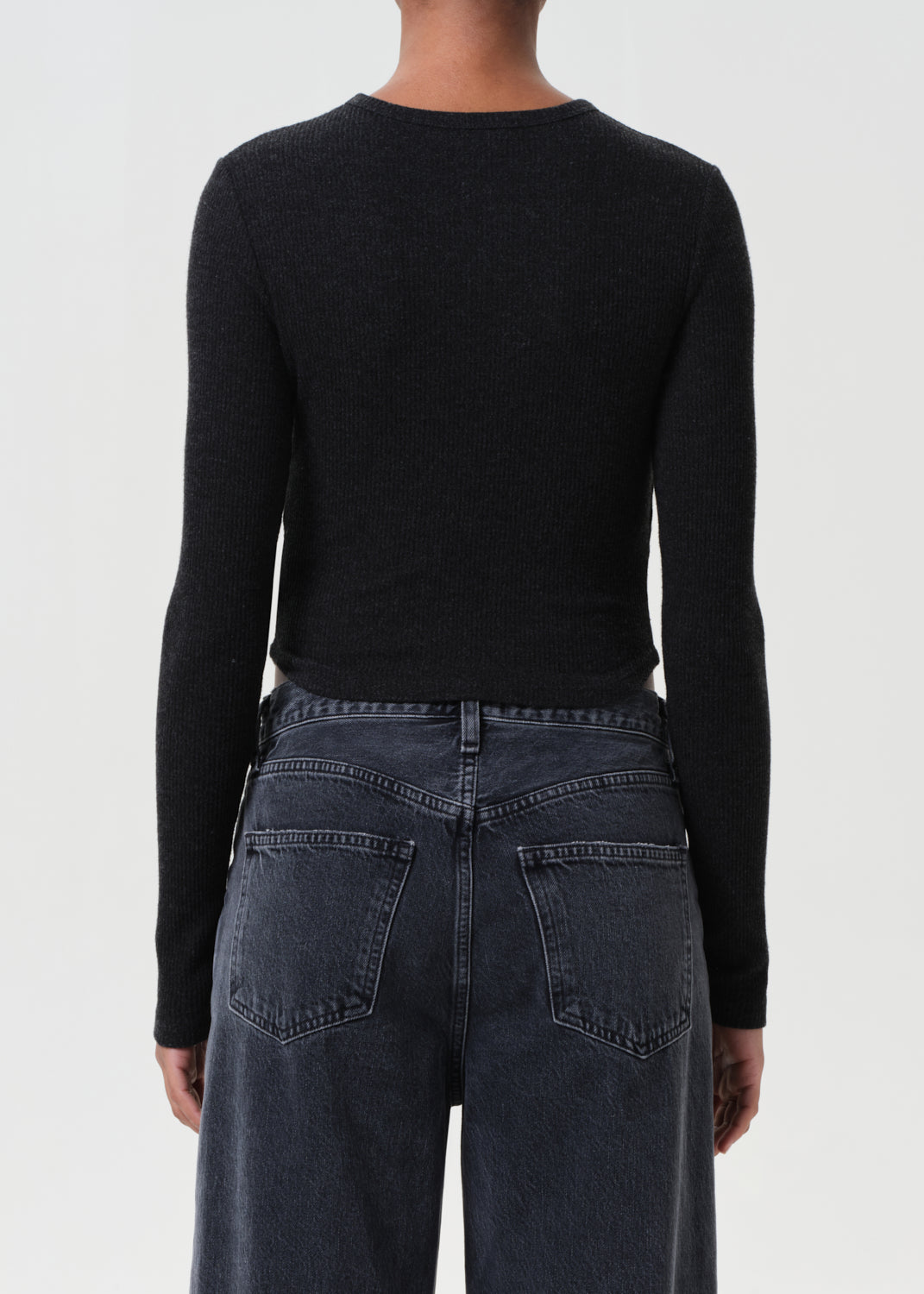 Person wearing a black long-sleeve top and dark jeans on a white background