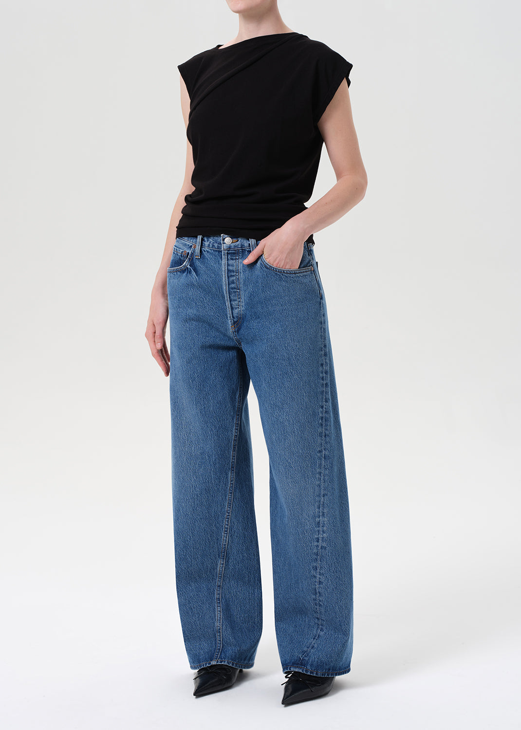 Person wearing a black sleeveless top and blue jeans on a white background