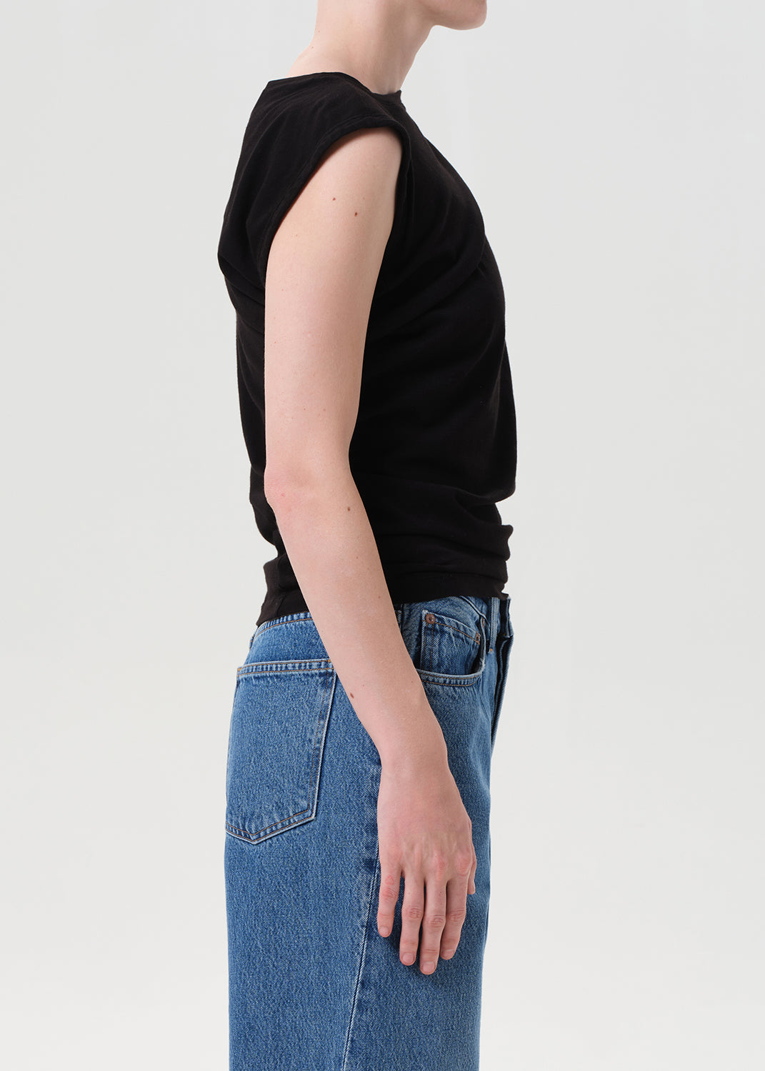 Person wearing a black sleeveless top and blue jeans on a light gray background