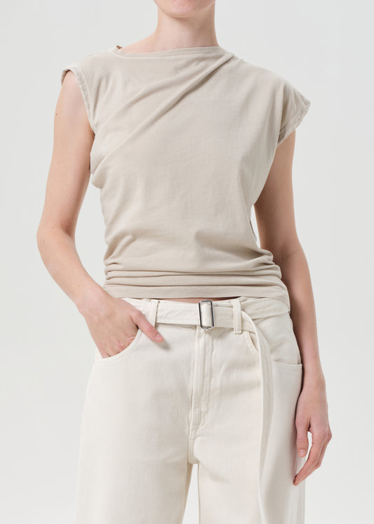 Person wearing a beige sleeveless top and white pants on a plain background