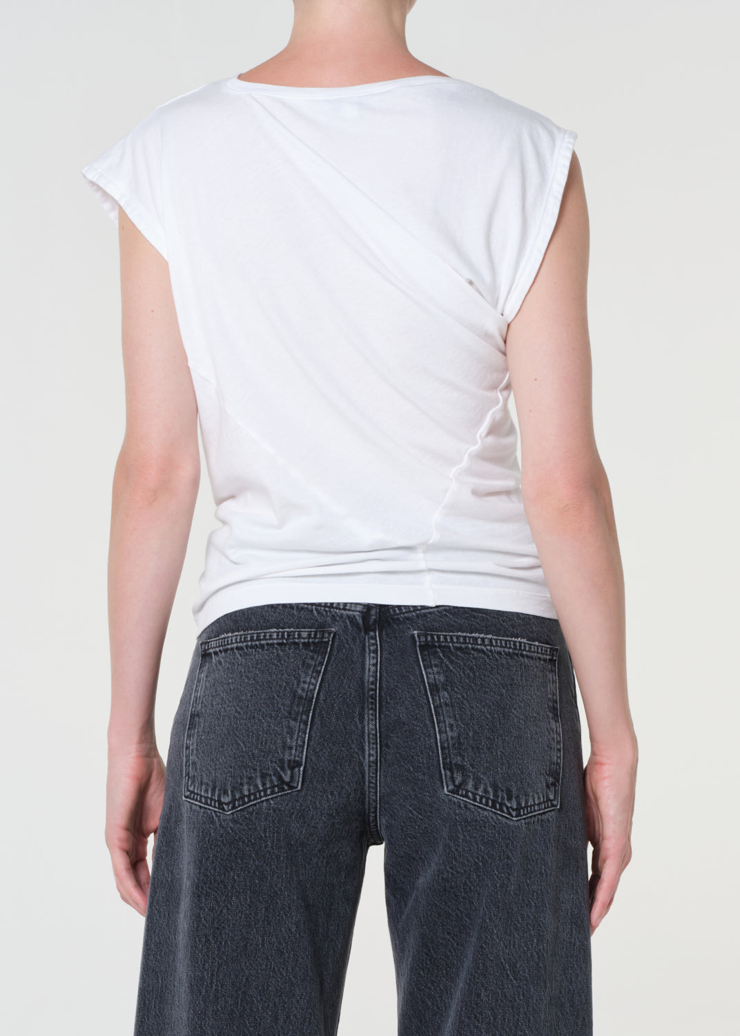 Person wearing a white sleeveless top and dark jeans on a plain background