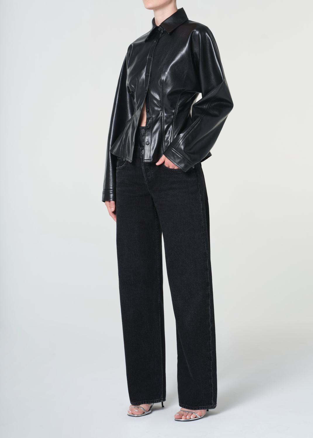 Person wearing a black glossy jacket and black pants on a white background