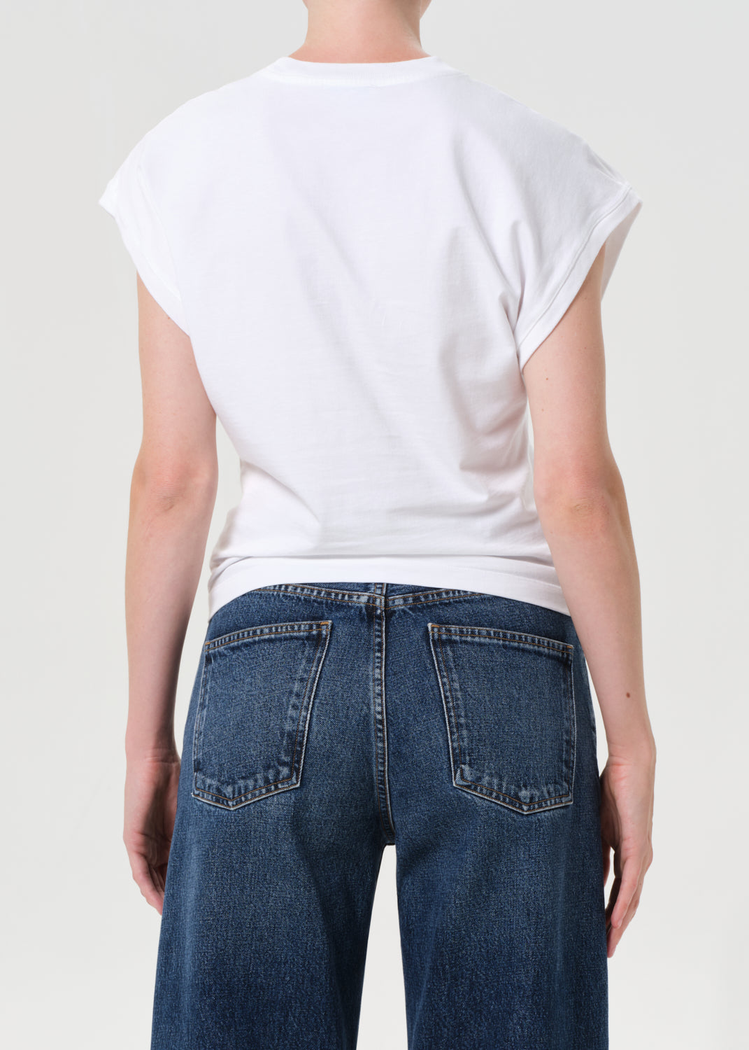 Person wearing a white t-shirt and blue jeans on a plain background