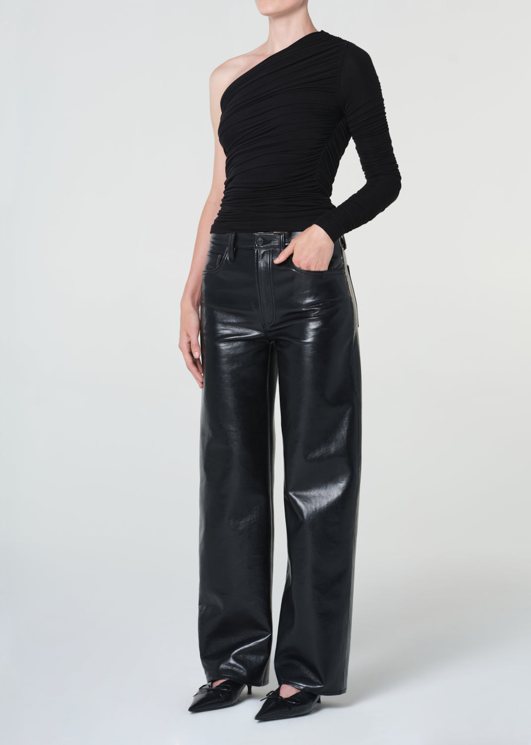 Person wearing a black one-shoulder top and black leather pants on a white background