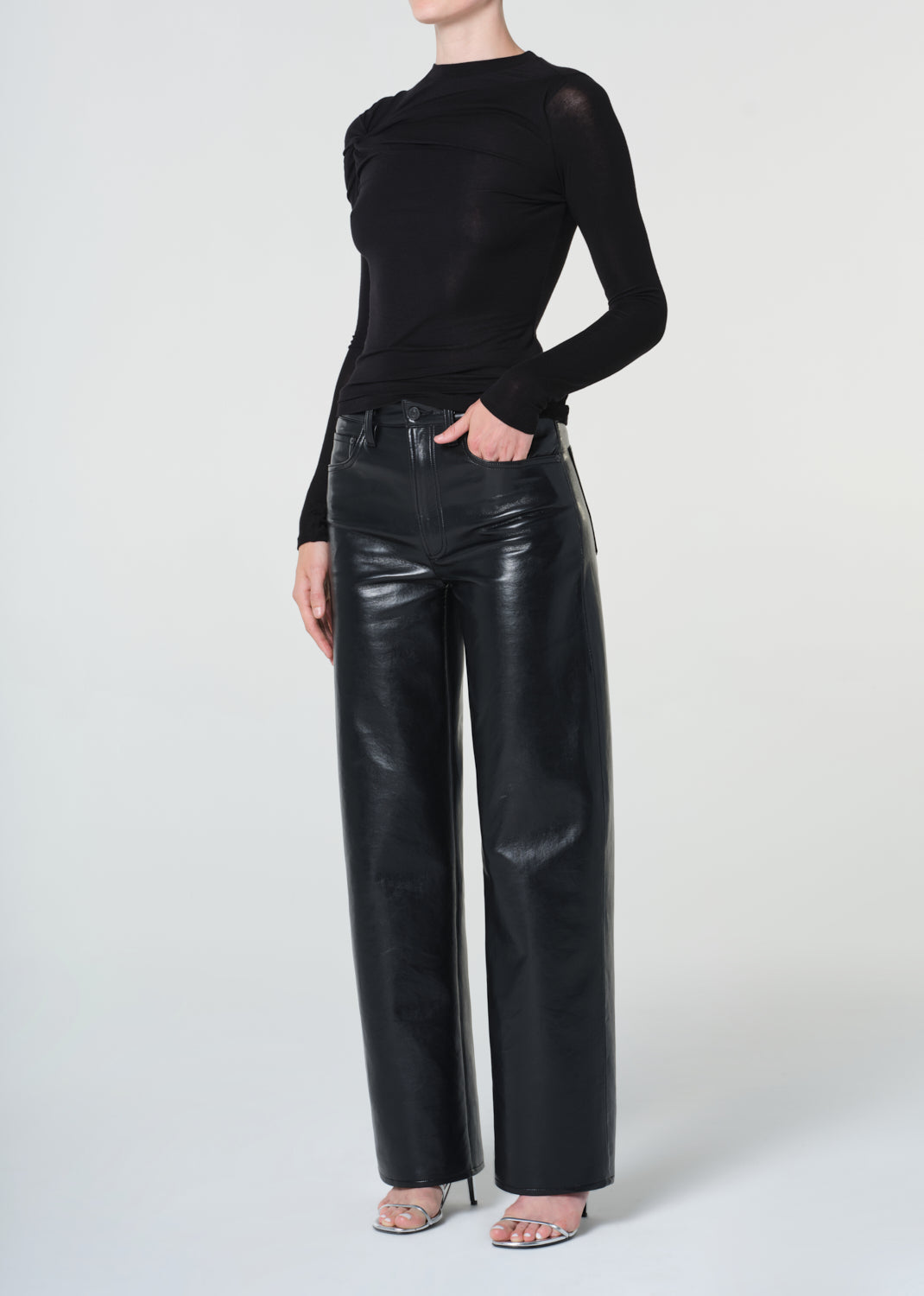 Person wearing a black long-sleeve top and black leather pants on a white background