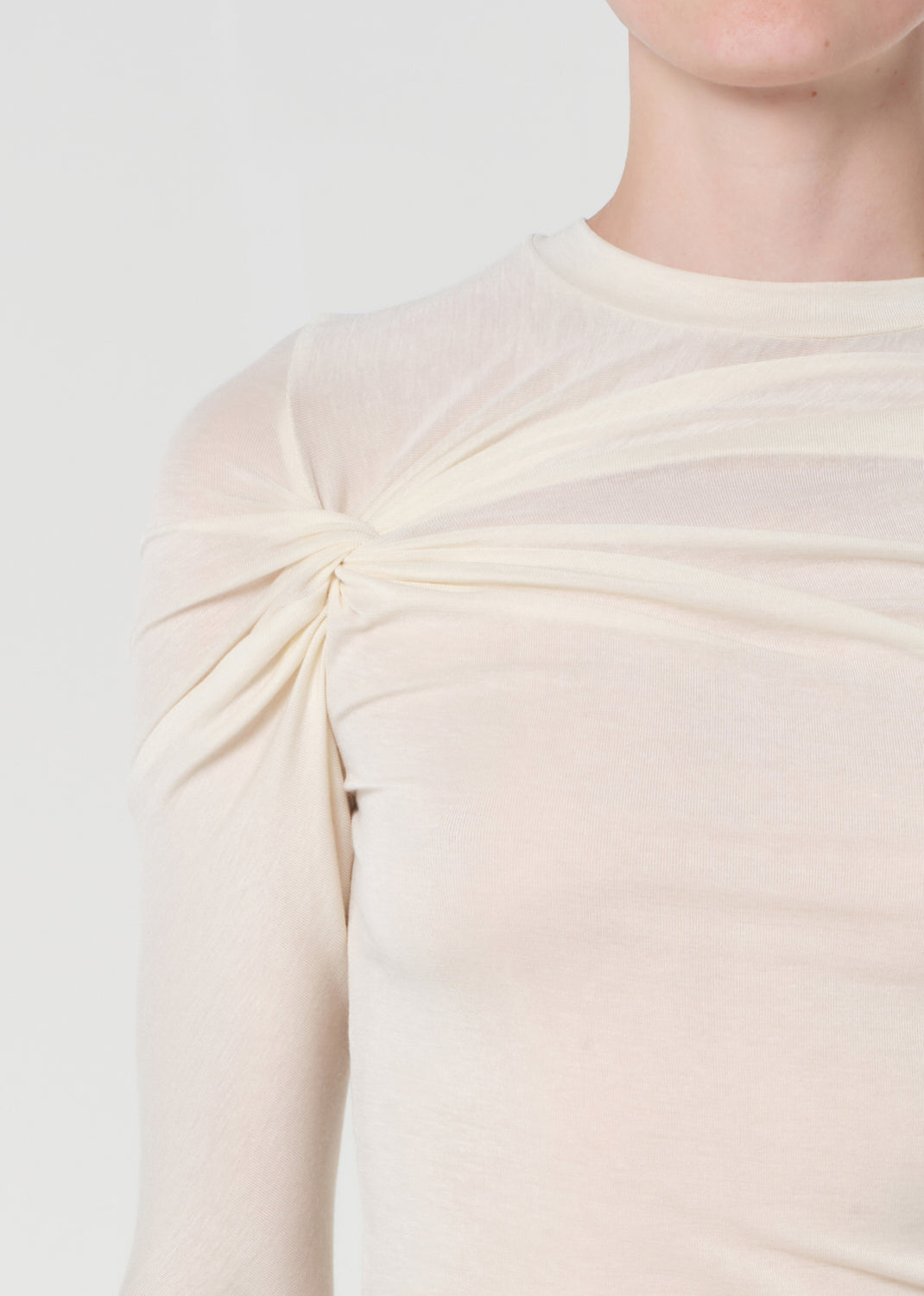 Close-up of a person wearing a light-colored dress with a knot detail on a plain background