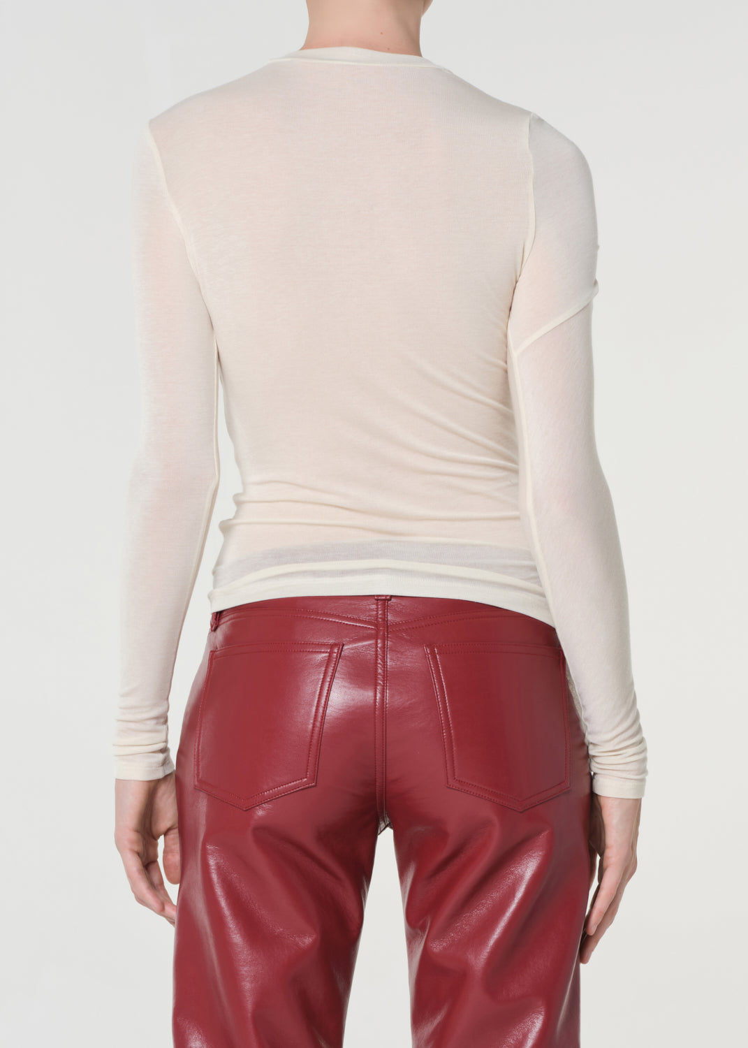 Person wearing a beige long-sleeve top and red leather pants on a white background