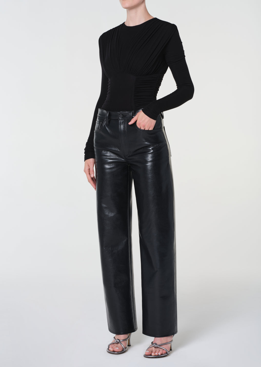 Person wearing black leather pants and a black long-sleeve top on a white background