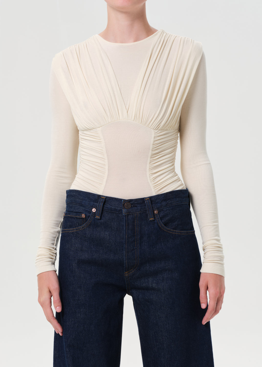 Person wearing a cream ribbed long-sleeve top and dark blue jeans on a white background