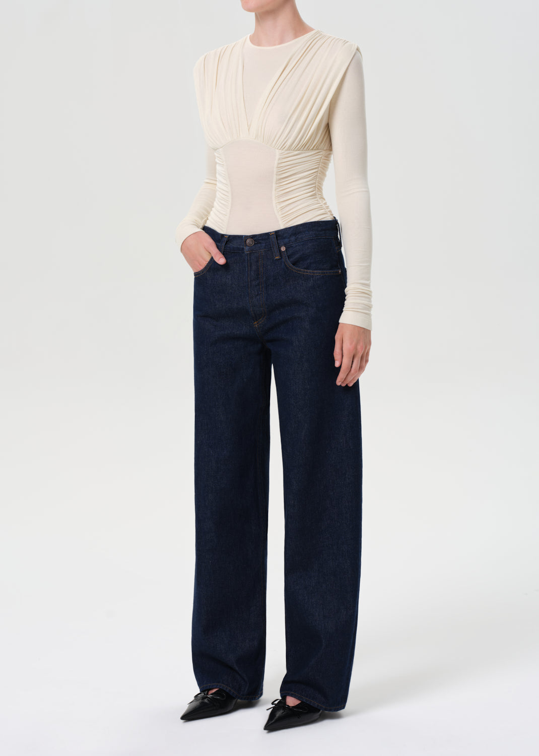 Person wearing a cream long-sleeve top and dark blue jeans on a white background