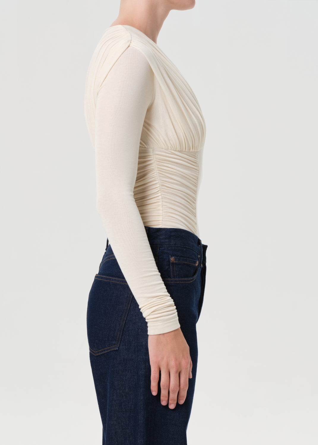 Person wearing a cream long-sleeve top and dark jeans on a light gray background