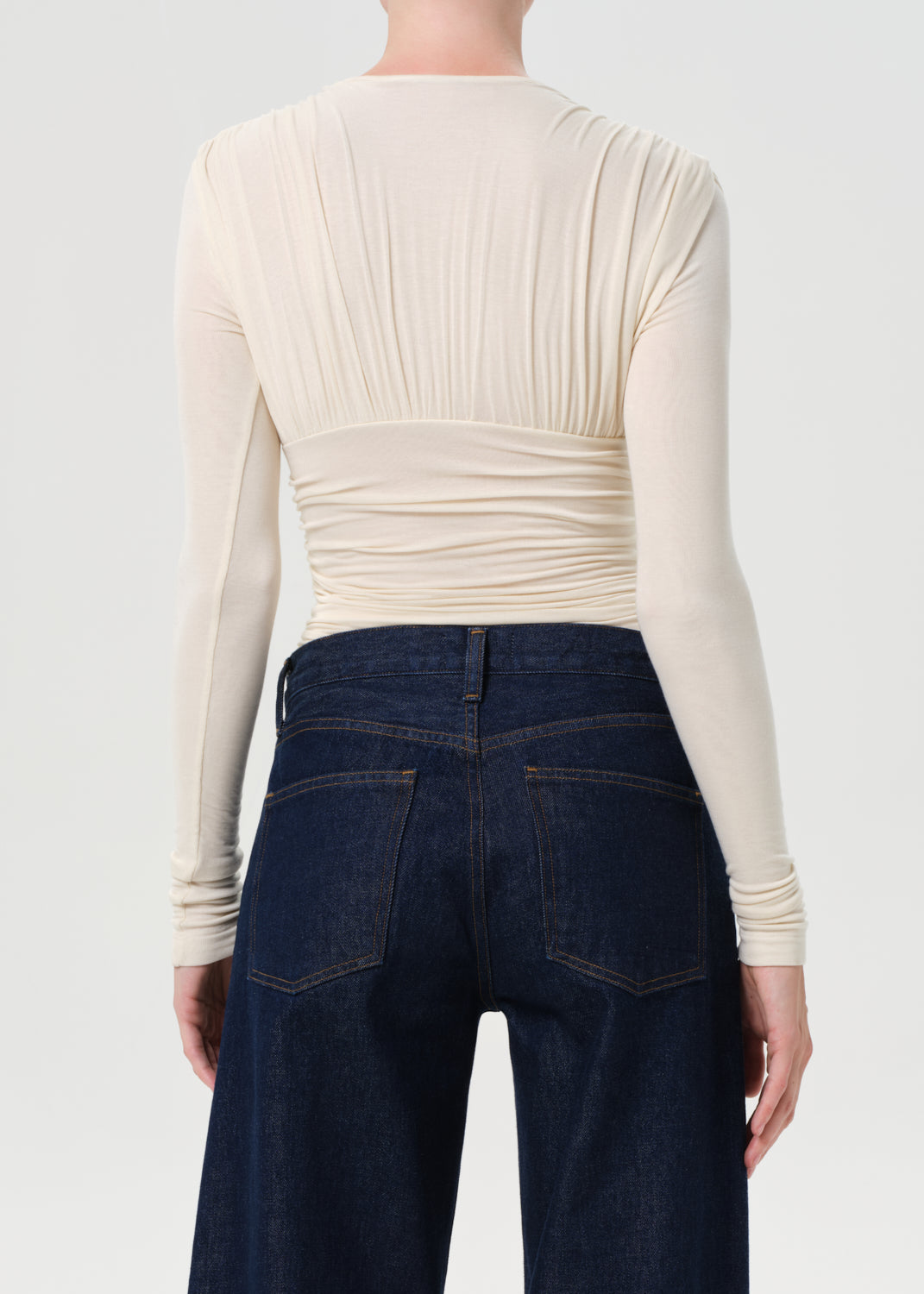 Person wearing a cream long-sleeve top and dark blue jeans on a light gray background