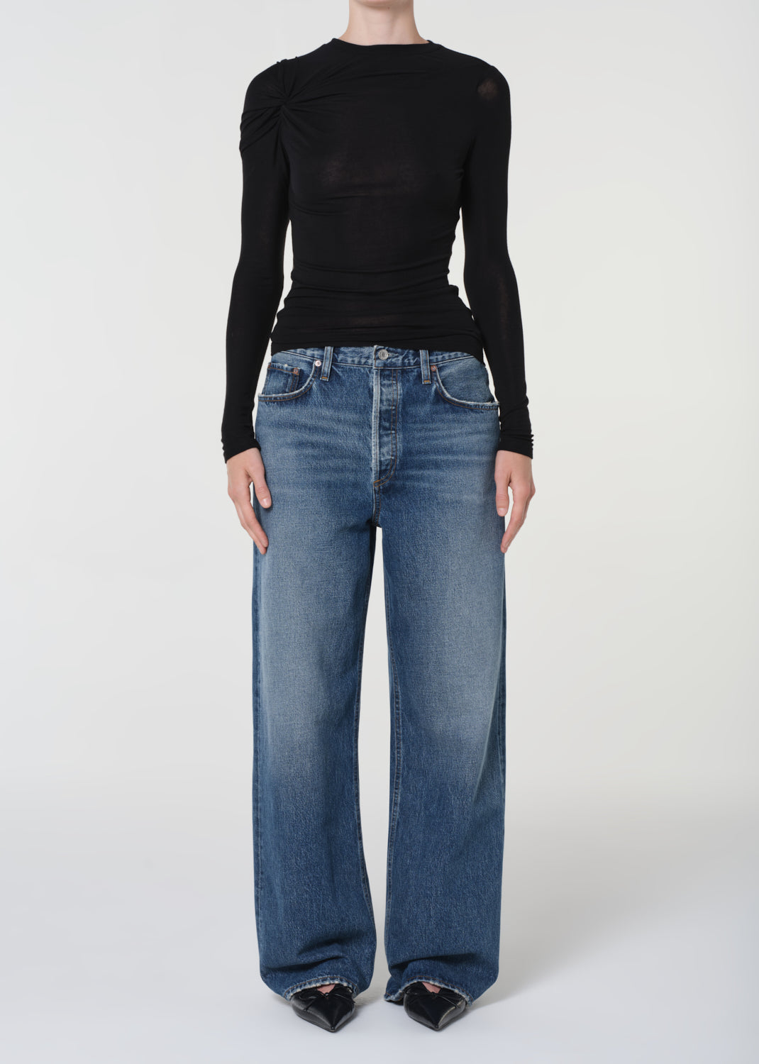 Person wearing a black long-sleeve top and blue jeans on a white background