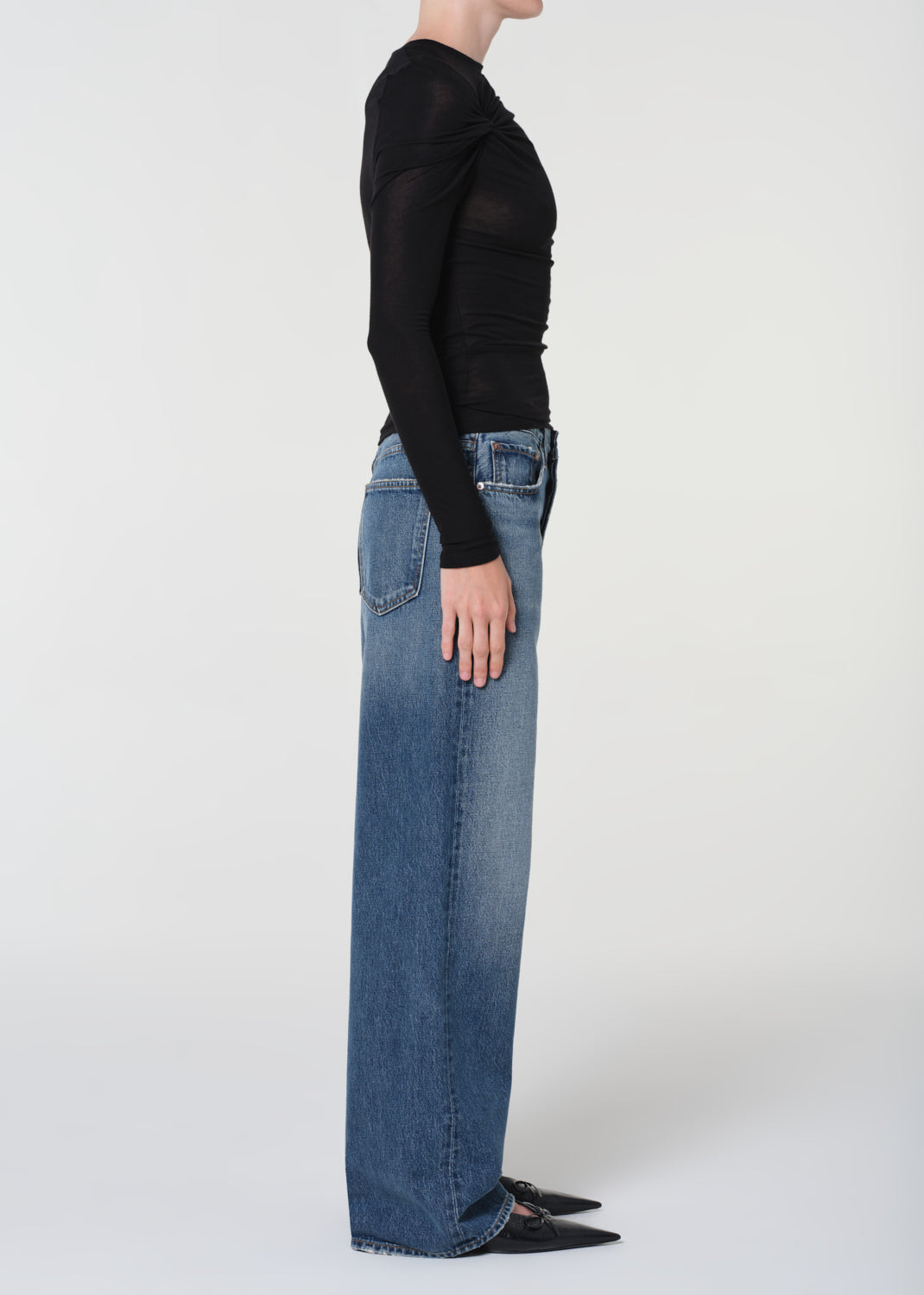 Person wearing blue jeans and a black top on a white background
