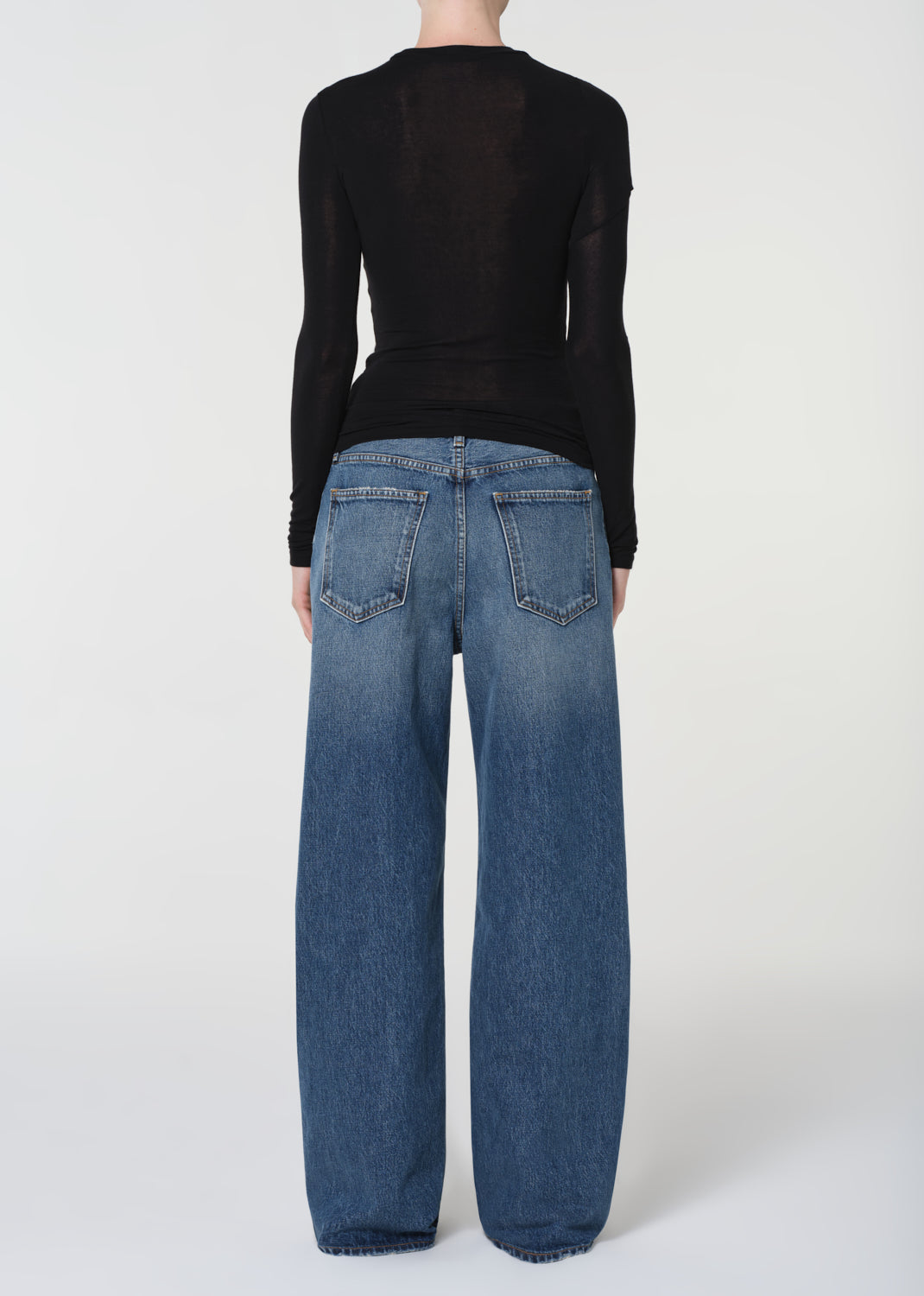 Person wearing blue jeans and a black top on a white background