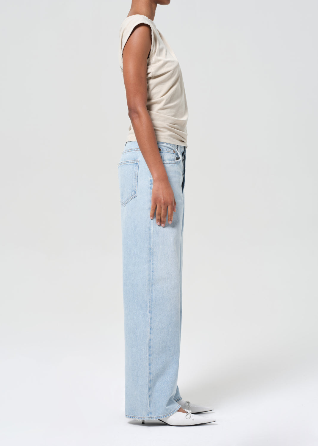 Person wearing light blue jeans and a beige top on a white background