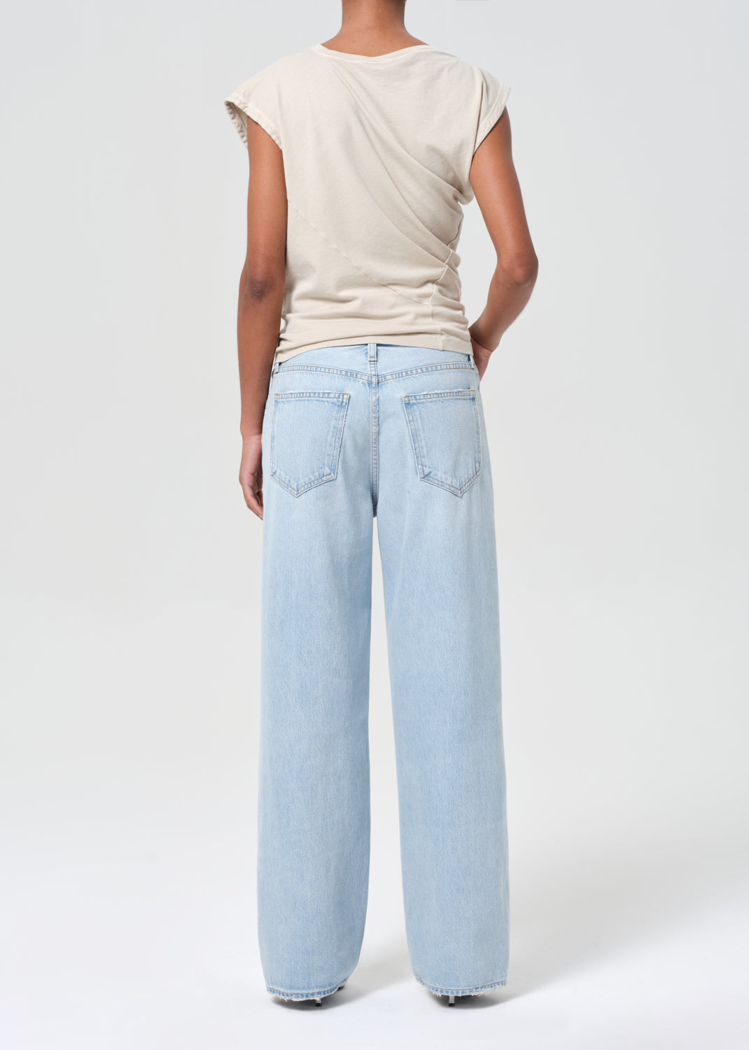 Person wearing light blue jeans and a beige top on a white background