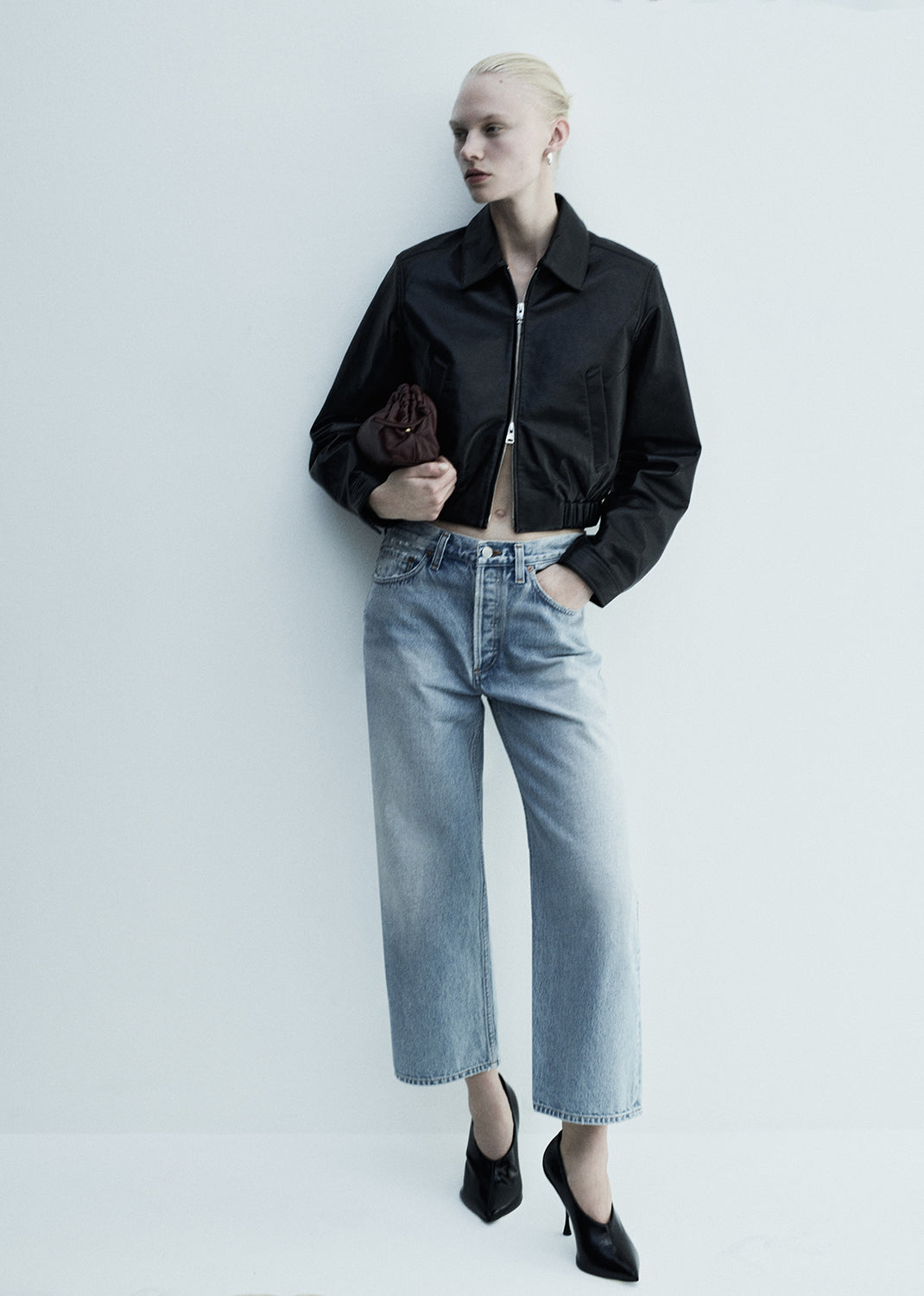 Person wearing a black jacket, light blue jeans, and black shoes on a white background