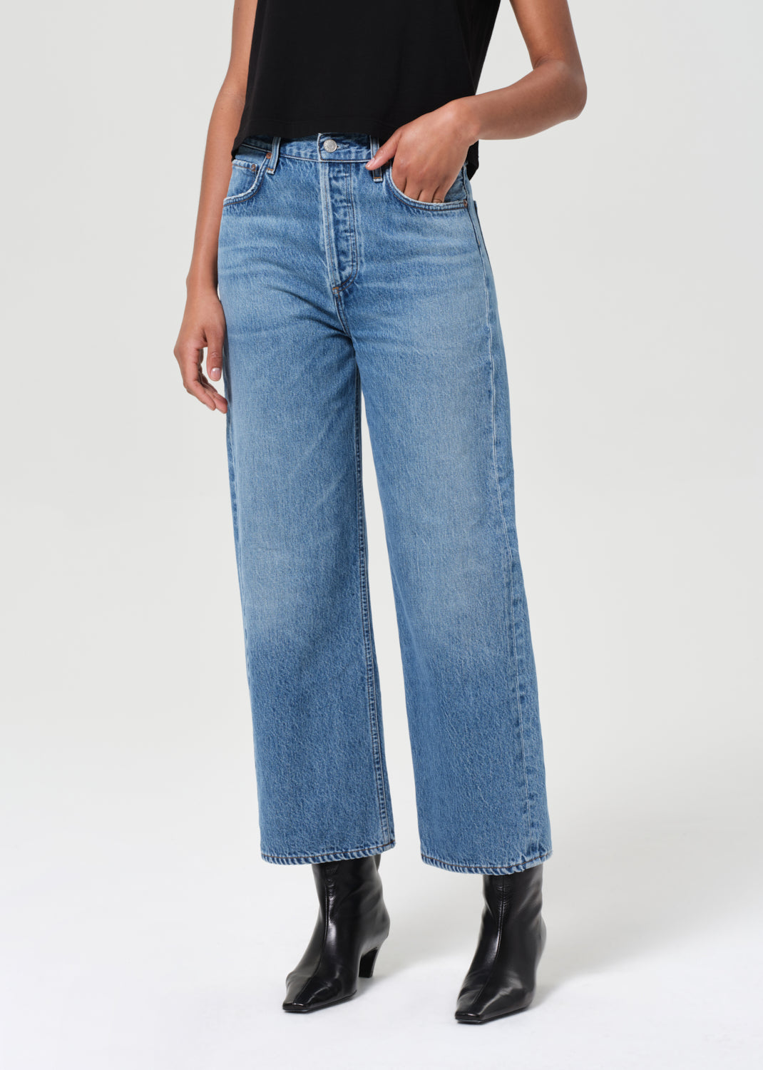 Person wearing blue jeans and black boots on a white background