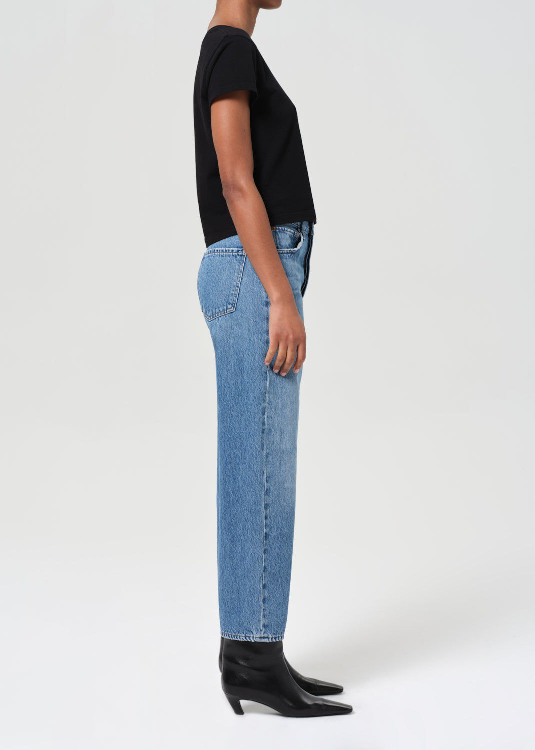 Person wearing blue jeans and black shoes on a white background