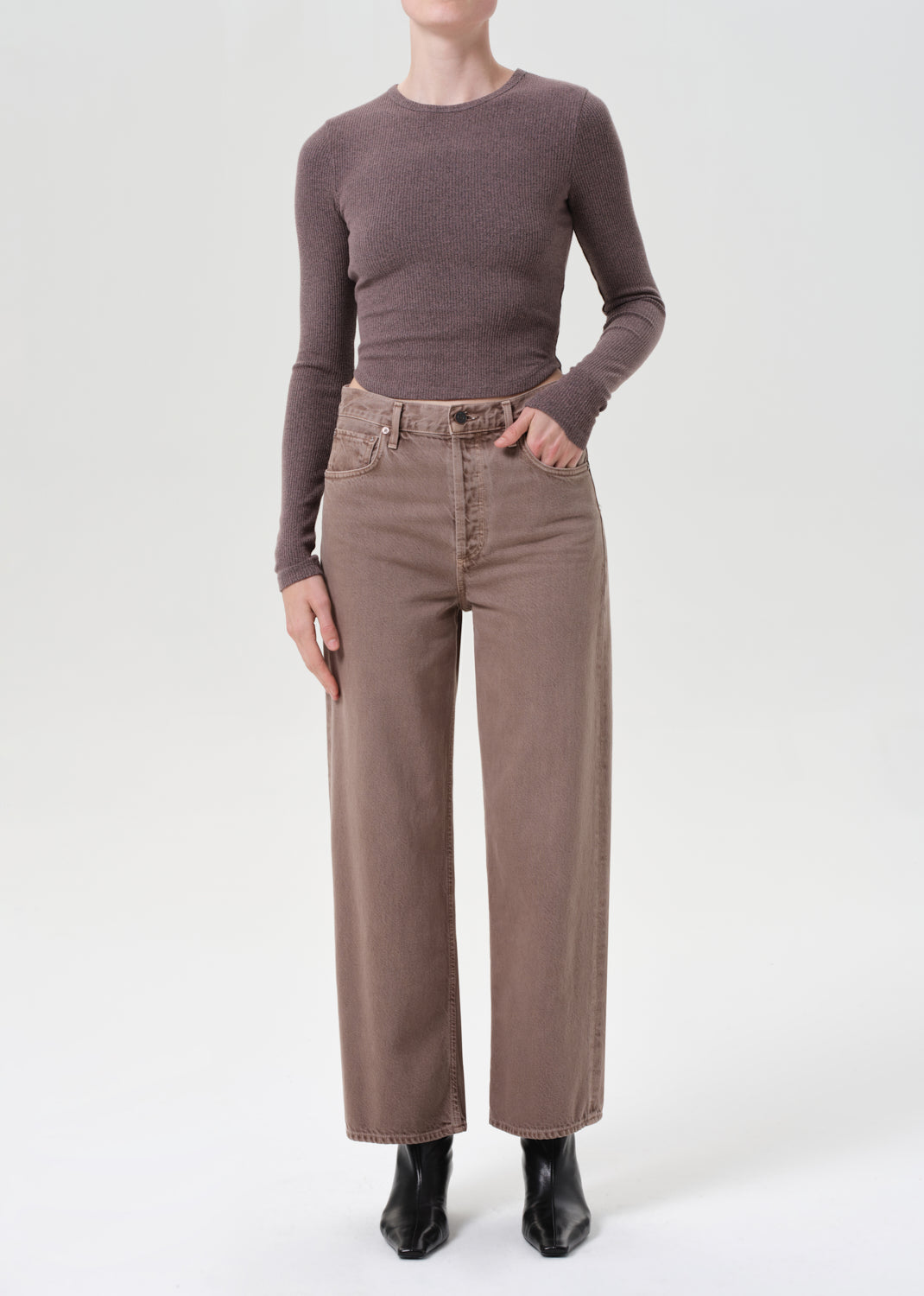 Person wearing a brown long-sleeve top and beige pants on a white background