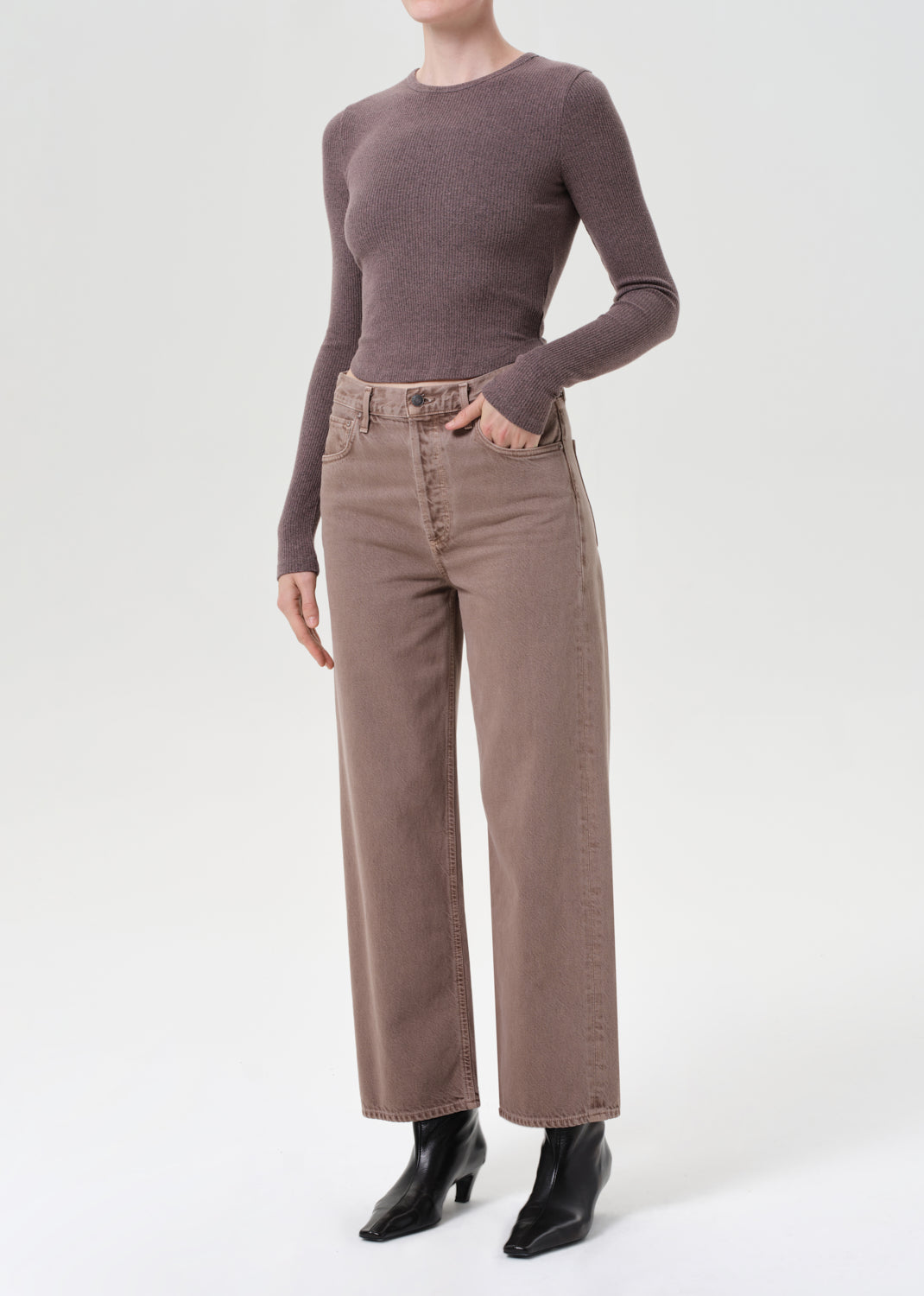 Person wearing a brown sweater and beige pants on a white background