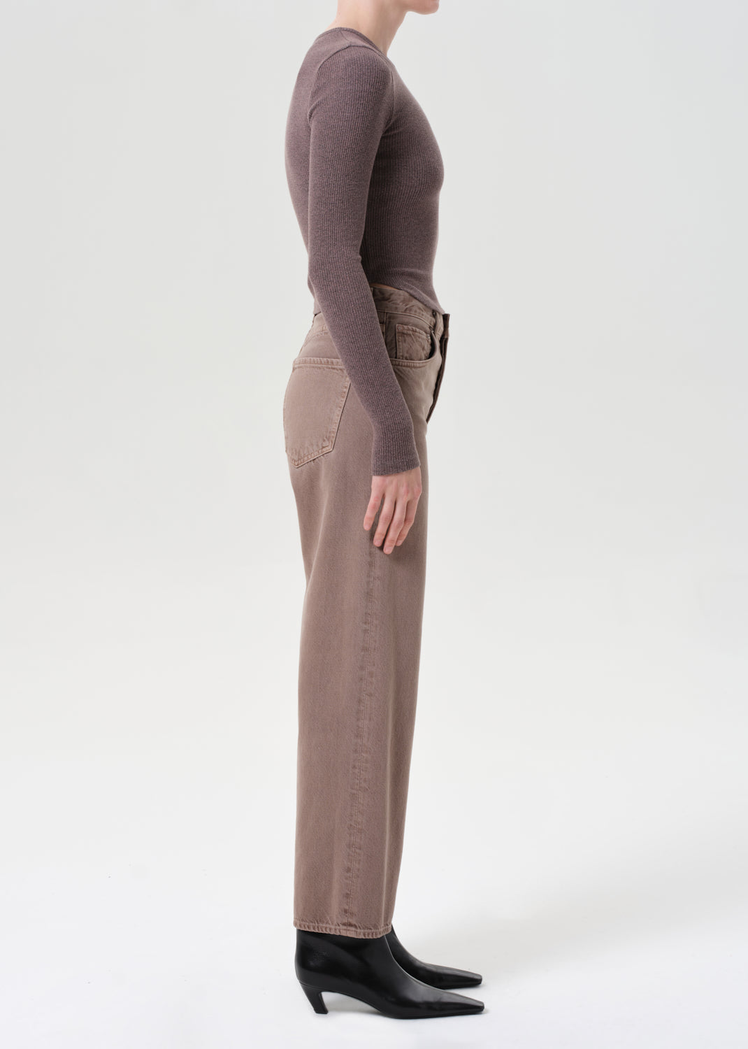 Person wearing a brown long-sleeve top and pants with black shoes on a white background