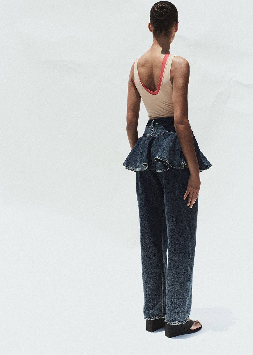 Person wearing a beige top and dark blue jeans with ruffled details on a white background