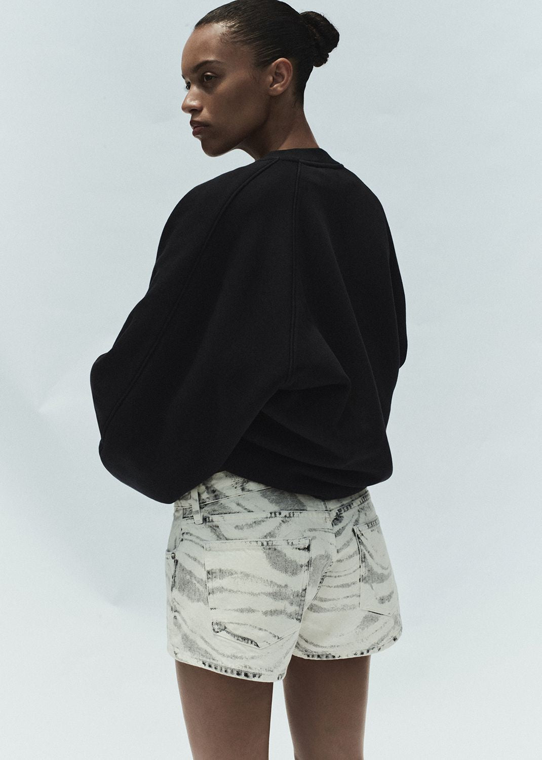 Person wearing a black sweater and patterned shorts on a plain background