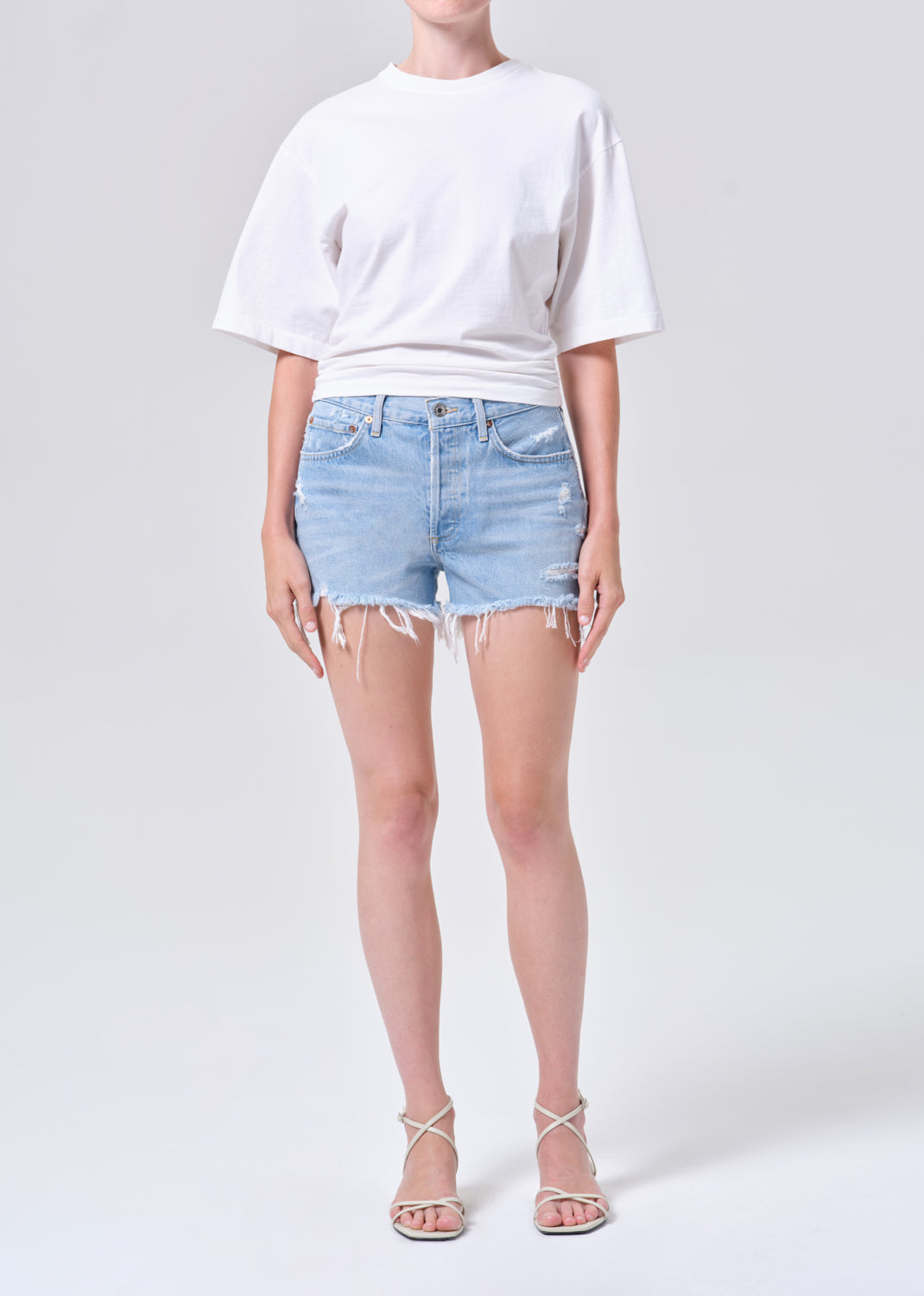 Person wearing a white t-shirt and light blue denim shorts on a plain background