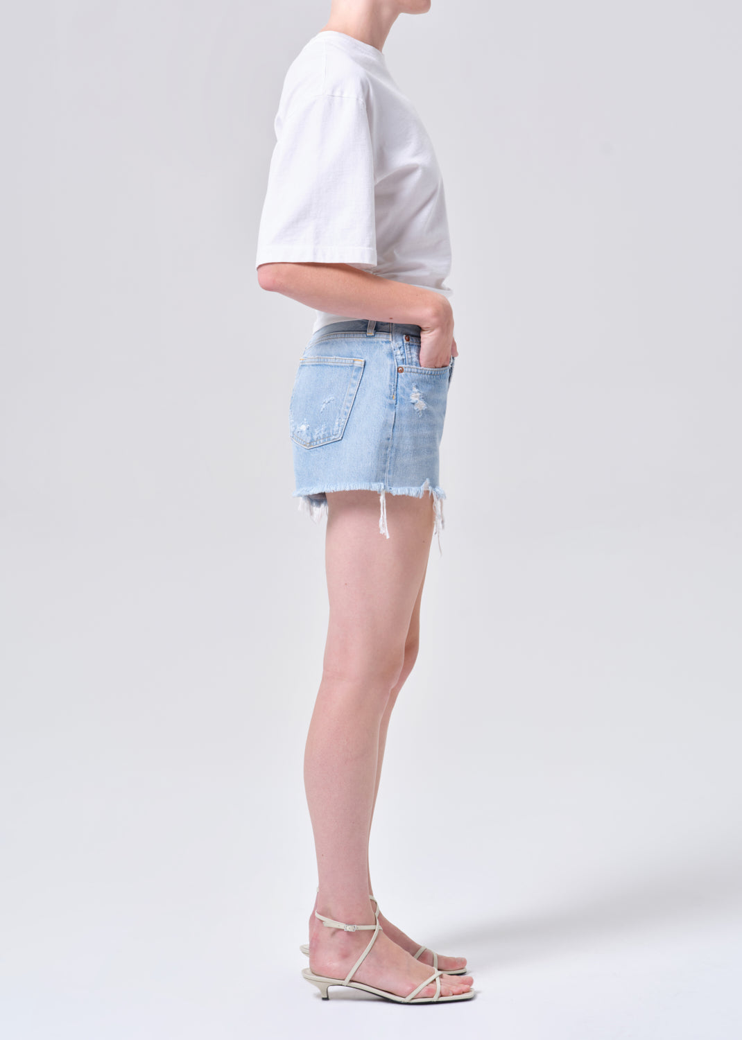 Person wearing a white t-shirt and light blue denim shorts on a plain background
