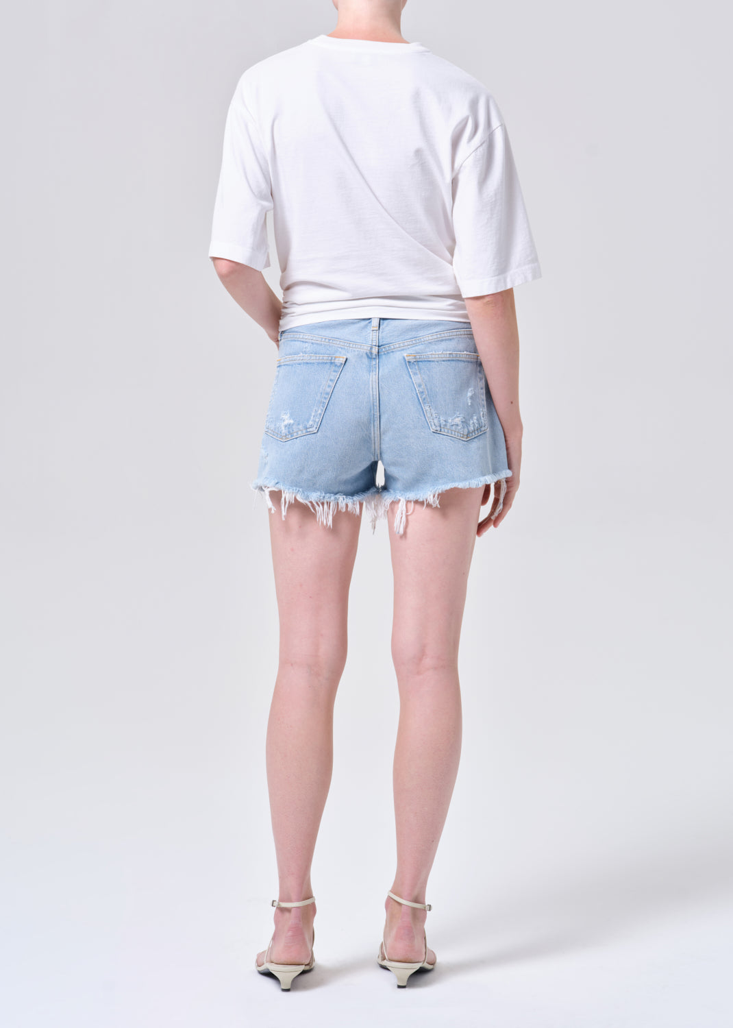Person wearing a white t-shirt and light blue denim shorts on a plain background