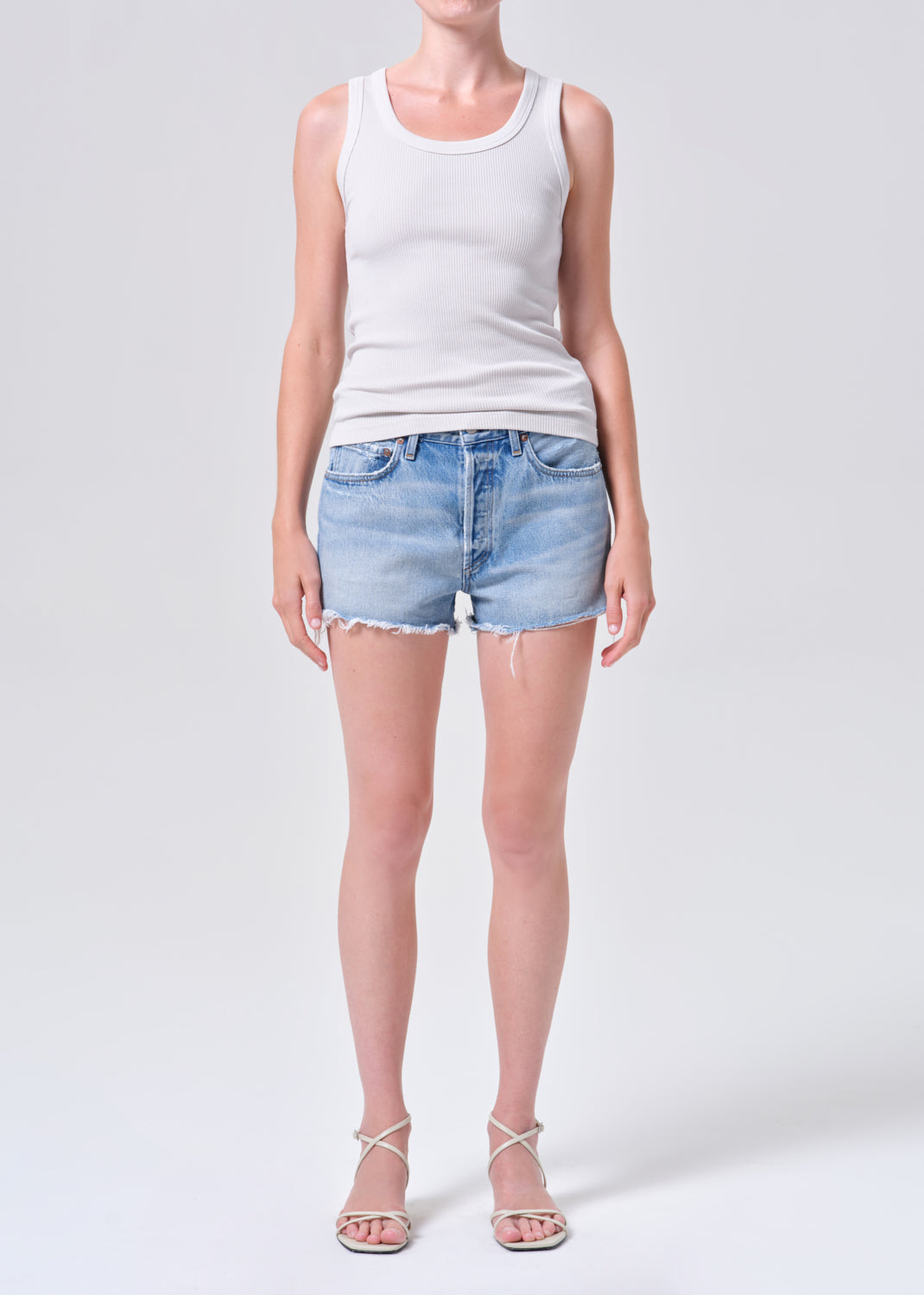 Person wearing a white tank top and light blue denim shorts on a white background