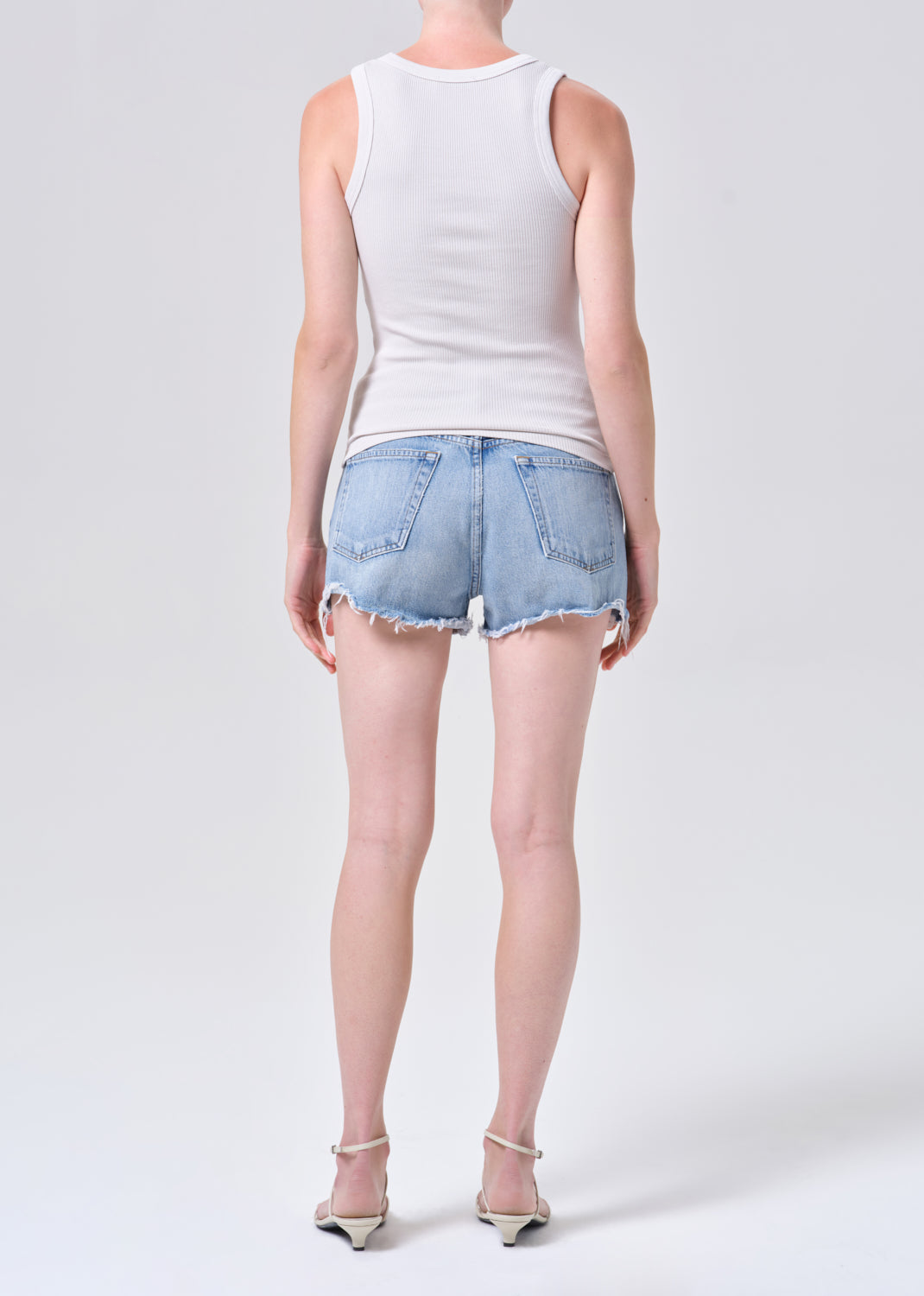 Person wearing a white sleeveless top and denim shorts on a white background