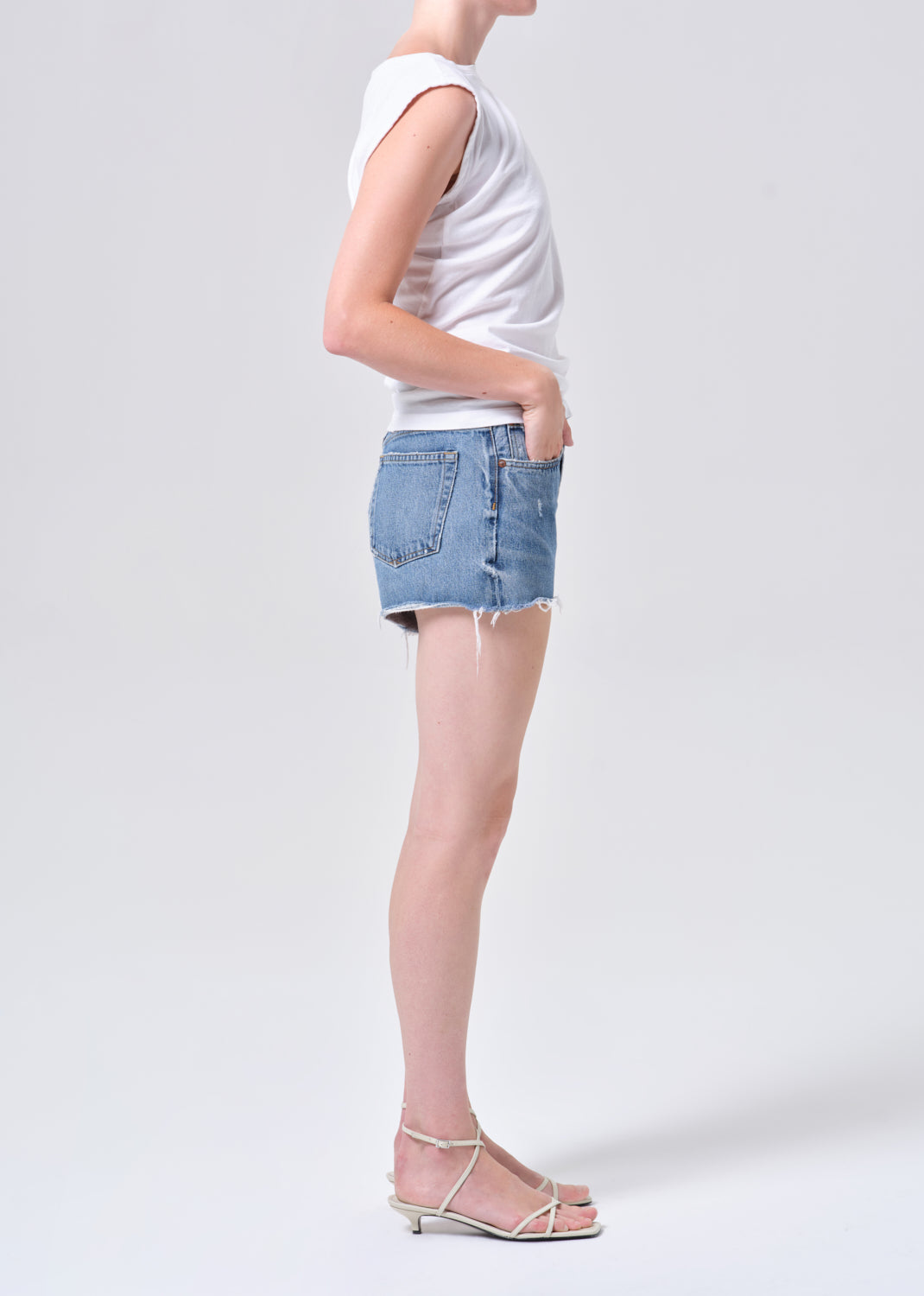 Person wearing a white sleeveless top and blue denim shorts on a light gray background