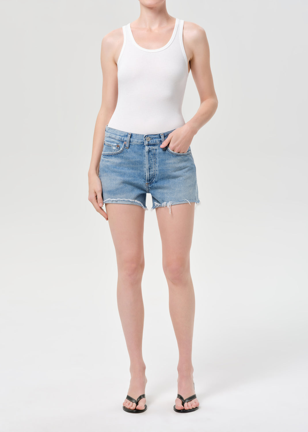 Person wearing a white tank top and denim shorts on a white background