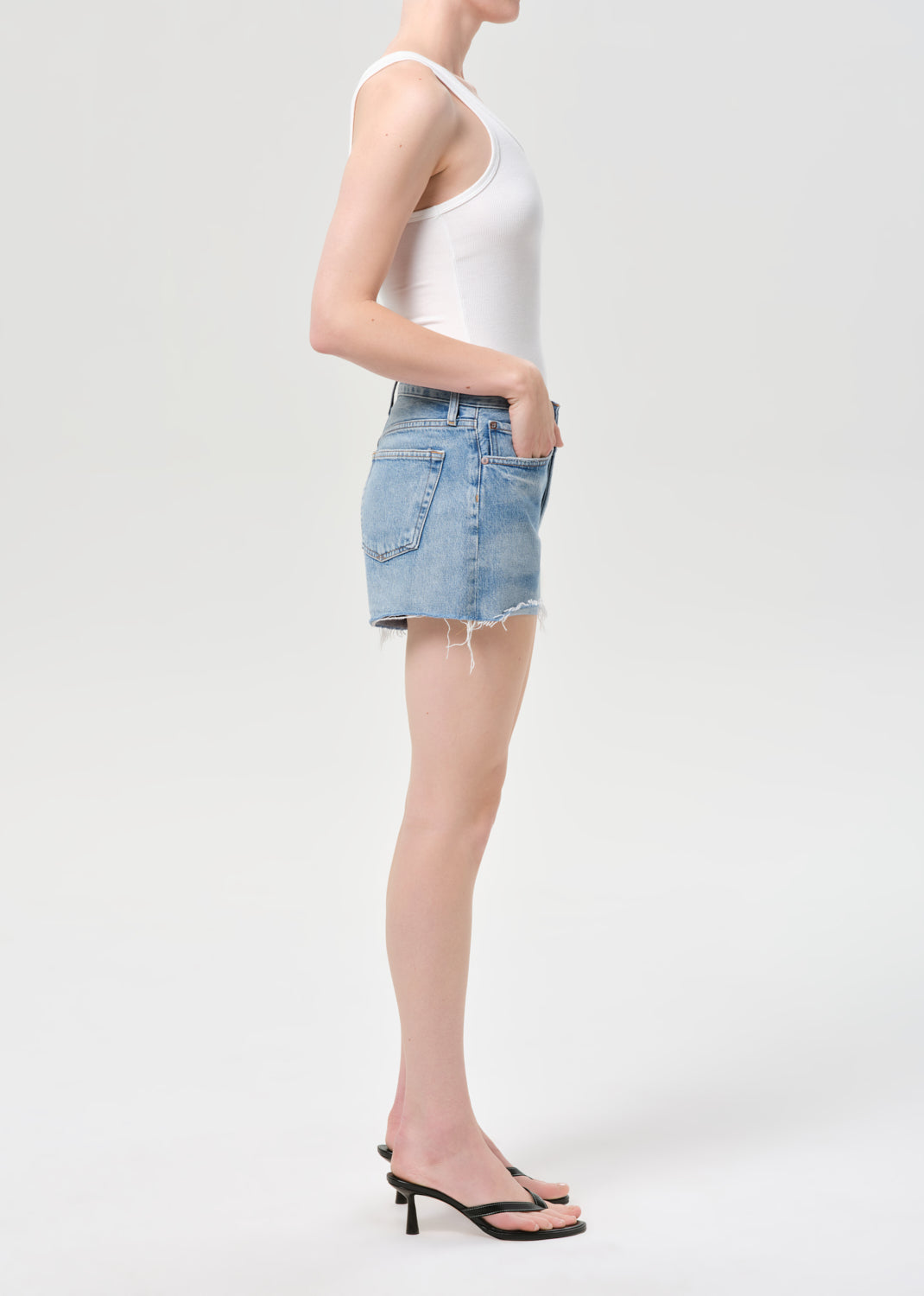 Person wearing a white tank top and light blue denim shorts on a white background