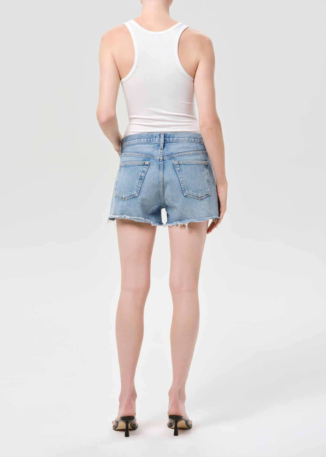 Person wearing a white tank top and light blue denim shorts on a white background