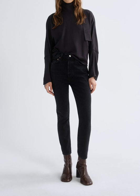 Person wearing a black long sleeve turtleneck sweater with black skinny jeans and brown ankle boots on a grey background