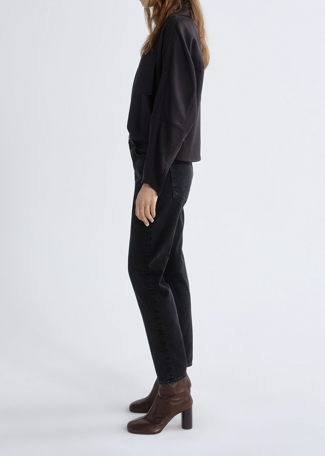 Person wearing a black long sleeve turtleneck sweater with black skinny jeans viewed from the side on a grey background