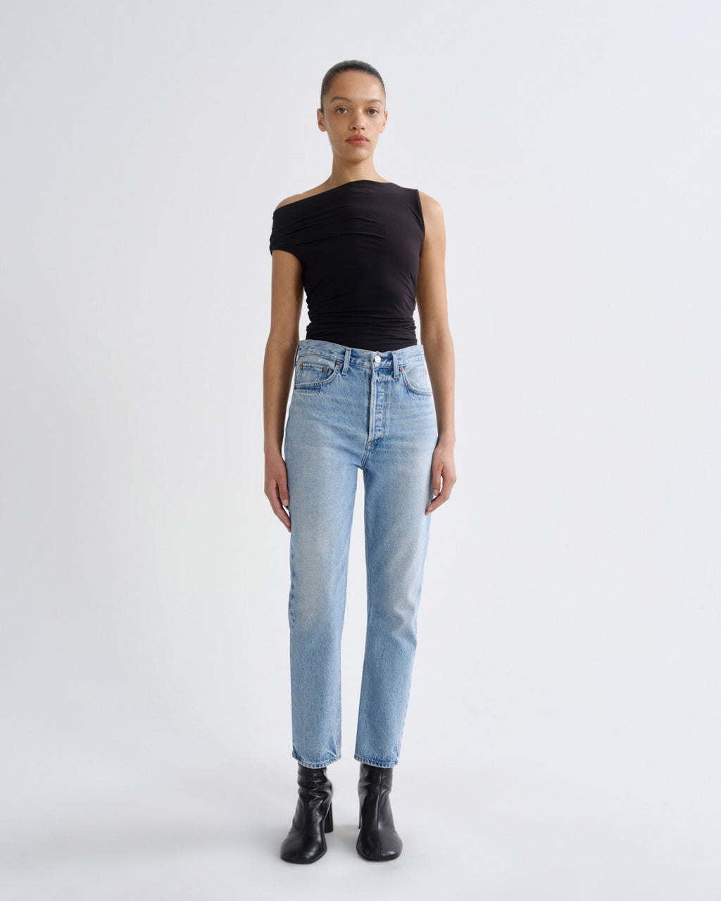 Person wearing a black top and light blue jeans on a white background