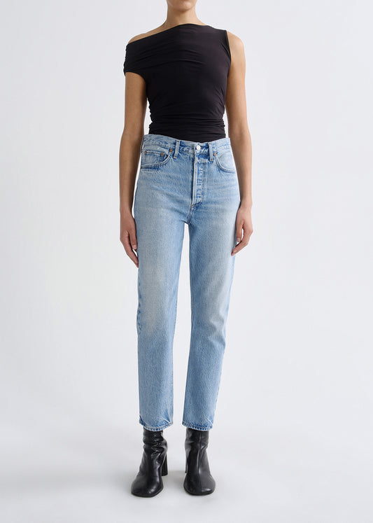 A model wearing light-wash blue straight-leg jeans, a black off-the-shoulder sleeveless top, and black ankle boots, photographed against a plain light gray studio background.