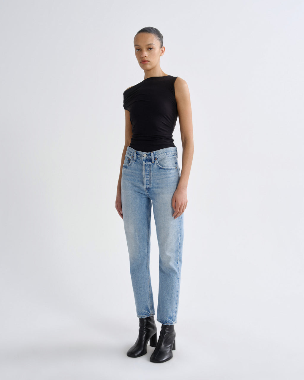 Person wearing a black sleeveless top and light blue jeans on a white background