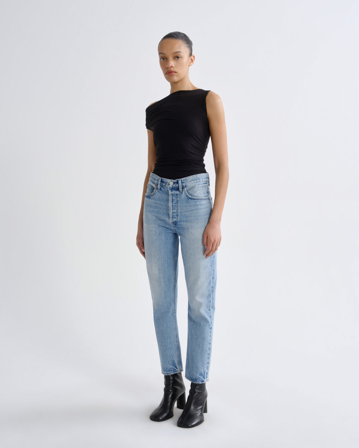 Person wearing a black sleeveless top and light blue jeans on a white background