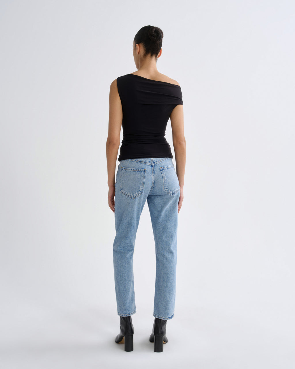 Person wearing light blue jeans and a black top on a white background