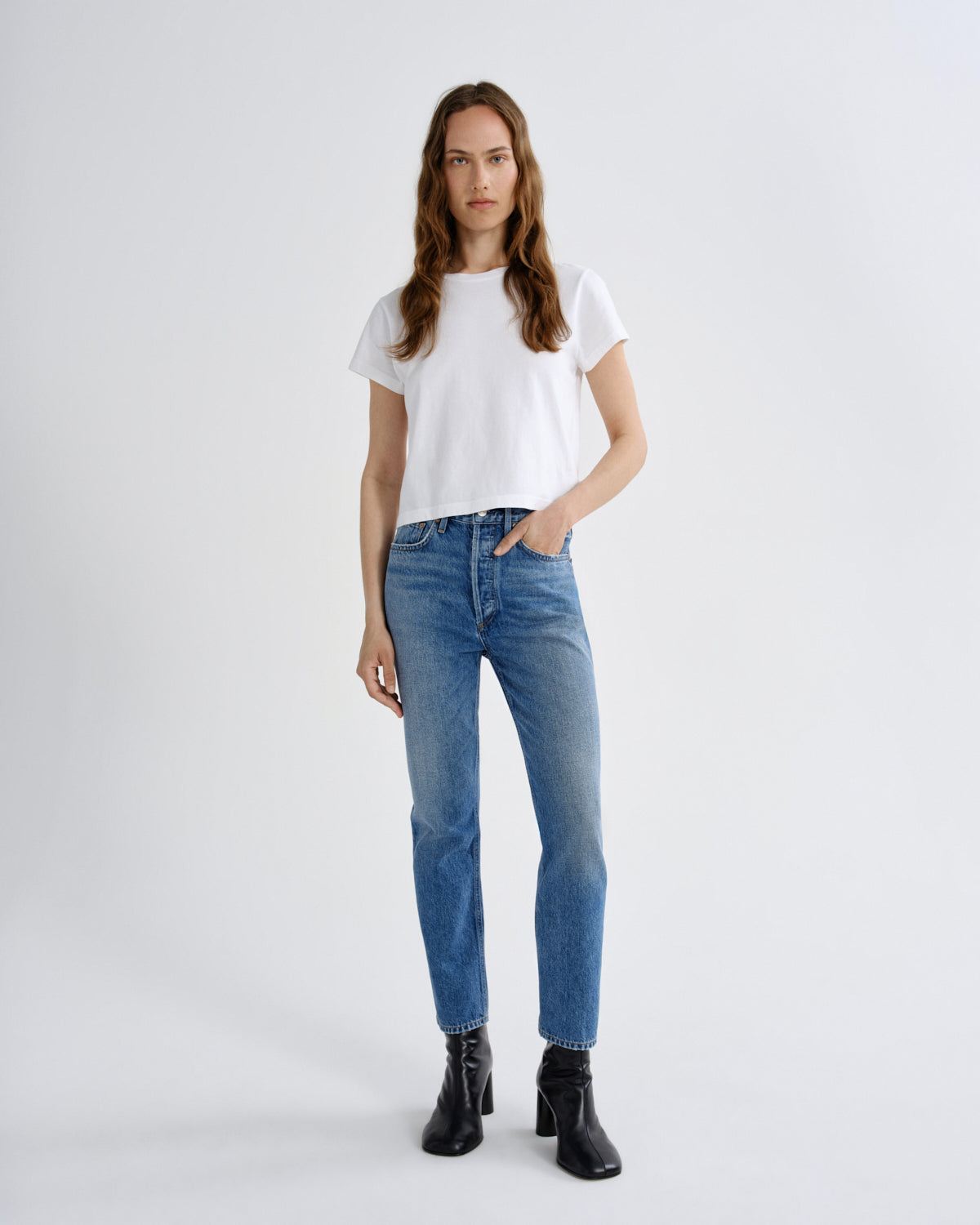 Person wearing a white t-shirt and blue jeans on a plain background
